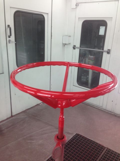 1964 Ford Fairlane - A red steering wheel is shown in a paint booth, ready for installation or repair.
