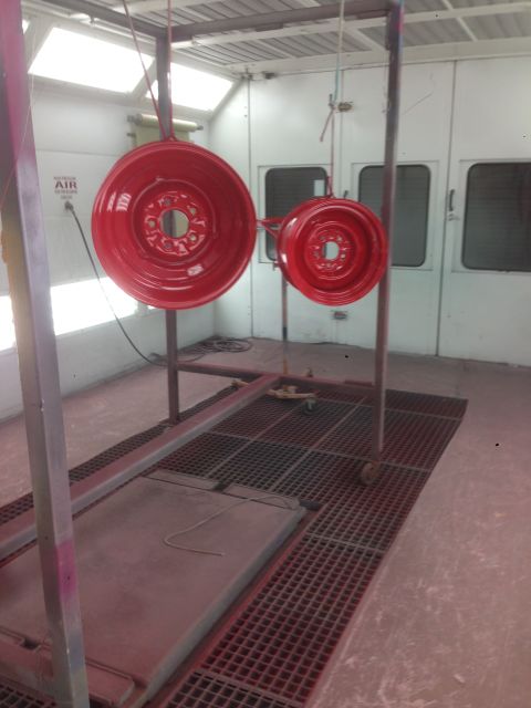 1964 Ford Fairlane - Two red wheels are being painted in a spray booth.