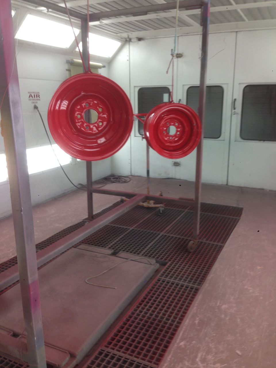 Two red painted wheels hanging in a paint booth
