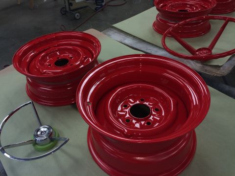 1964 Ford Fairlane - Several red painted steel wheels and a chrome steering wheel hub are laid out on a workbench.