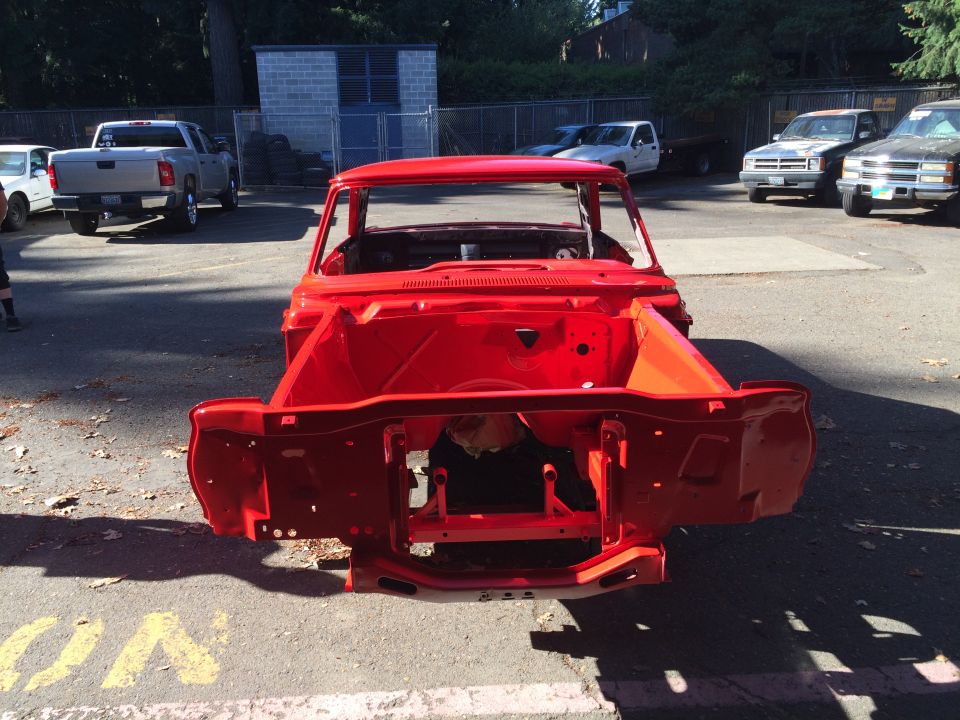 Red car body shell, front view, with other vehicles and a building in the background