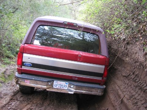 1989 Ford Bronco - This red Ford Bronco with a camper shell is stuck in a muddy off-road trail.