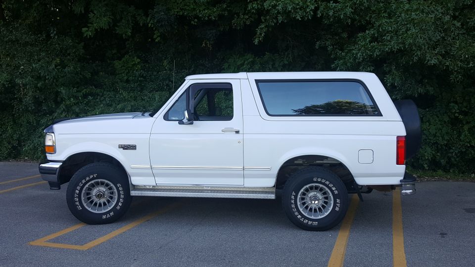 Side view of a white Ford Bronco parked in a lot with trees behind it