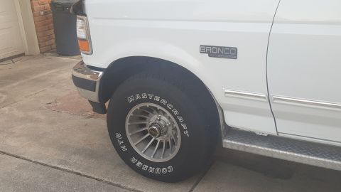 1995 Ford Bronco - Close-up of a white 1995 Ford Bronco's front fender and wheel assembly.