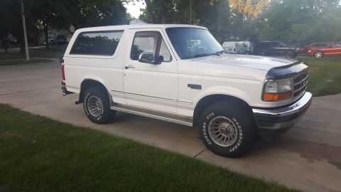 1995 Ford Bronco - A white Ford Bronco is parked on a concrete driveway next to a lawn.