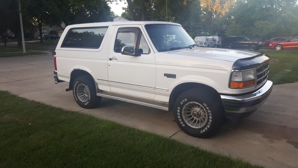 White Ford Bronco parked on a driveway. It has a black bug deflector on the hood