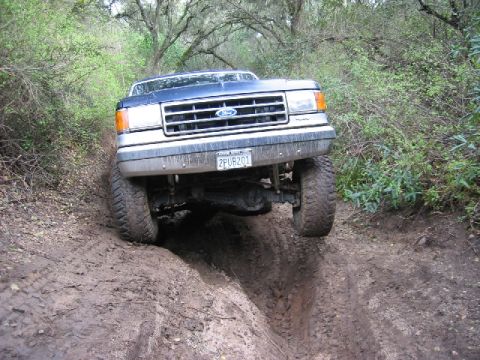 1989 Ford Bronco - Ford Bronco tackling a challenging off-road obstacle on a muddy track.