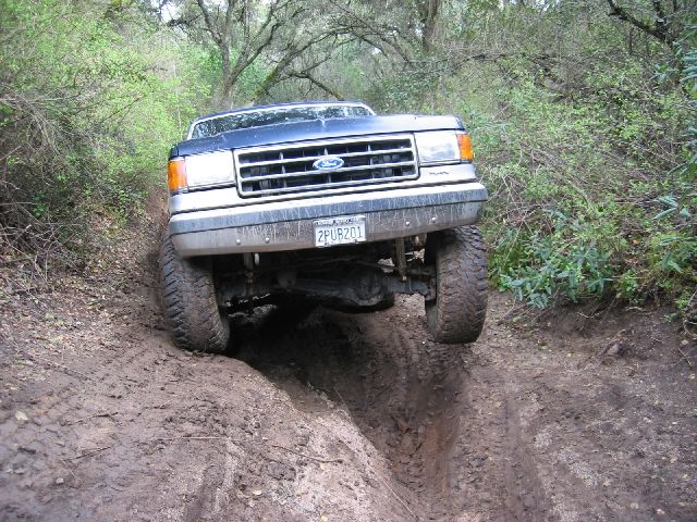 Blue-and-silver Ford 4x4 climbing a muddy rut, front view, plate 2PUB201