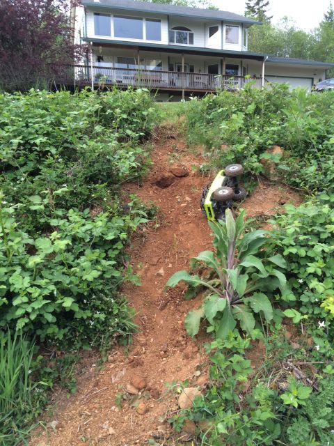 1989 Ford Bronco - A remote control vehicle has tipped over on a steep, overgrown dirt slope near a residential building.