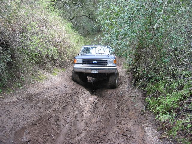 Lifted blue and silver Ford 4x4 driving down a deeply rutted muddy trail