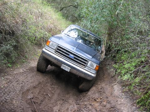 1989 Ford Bronco - A dark blue 1987 Ford Bronco navigates a challenging muddy off-road trail.