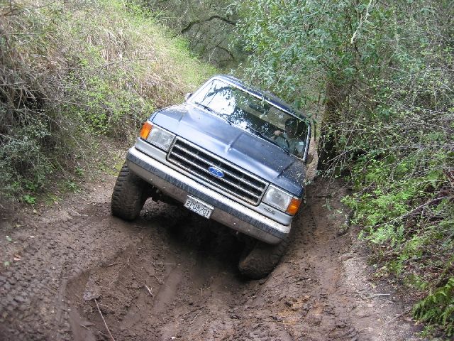 Blue-and-silver Ford SUV descending a rutted muddy trail, front 3/4 view