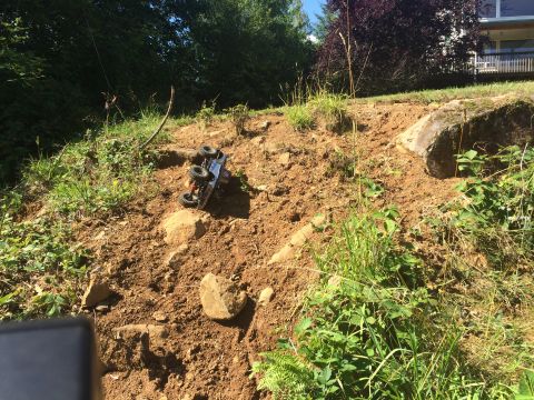 1989 Ford Bronco - A remote control truck is overturned on a steep, rocky slope with vegetation.