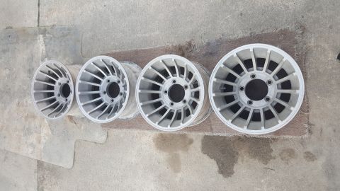 1995 Ford Bronco - Four aluminum alloy wheels are displayed on a textured surface, showing their intricate spoke patterns.
