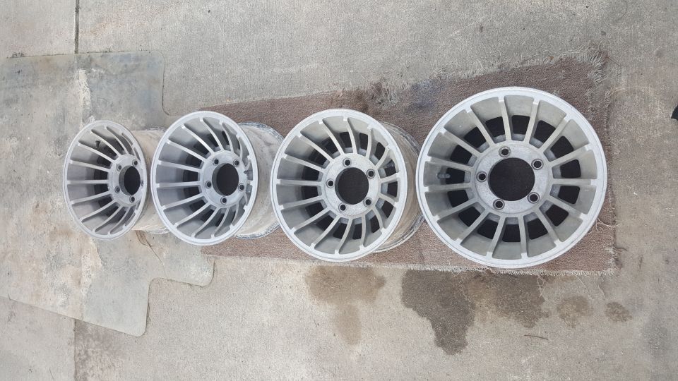 Four silver aluminum alloy wheels with a multi-spoke design are laid out on a concrete surface