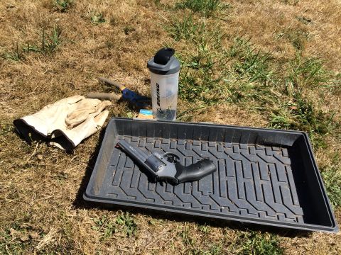 1989 Ford Bronco - A revolver rests in a tray on the grass, accompanied by gardening tools and a water bottle.