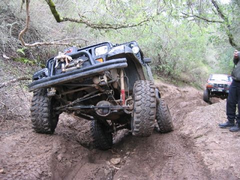 1989 Ford Bronco - Two off-road vehicles are shown on a muddy trail, one in the foreground and another further up the path.