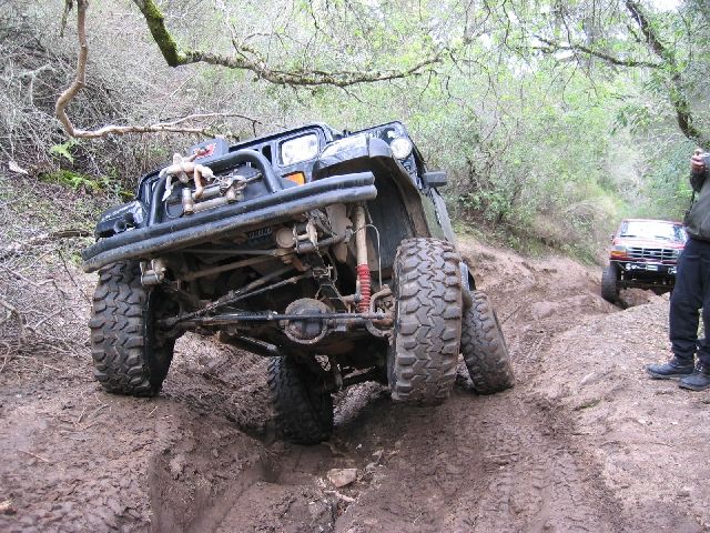 Dark lifted 4x4 flexing in deep mud ruts, solid front axle and red shocks exposed