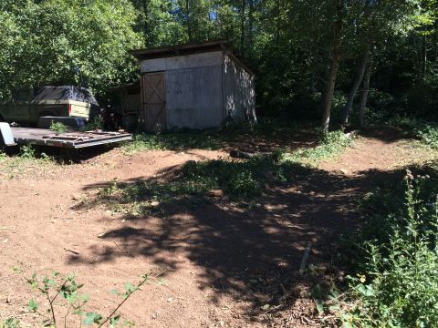 1989 Ford Bronco - An old pickup truck sits on a trailer next to a shed in a wooded area.