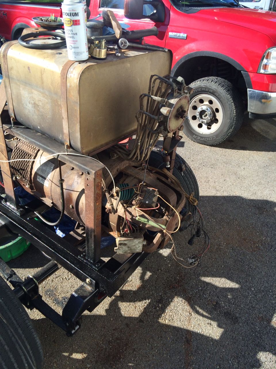 Bare vehicle chassis with fuel tank and wiring beside a red Ford Super Duty pickup