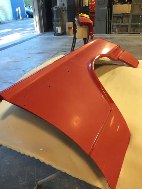1964 Ford Fairlane - A red fender, likely for a classic car, is shown in a workshop setting, possibly undergoing restoration or repair.