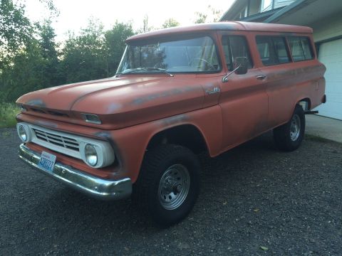 1962 Chevrolet Suburban - This 1962 Chevrolet Suburban has a faded orange paint job and is parked outside a garage.