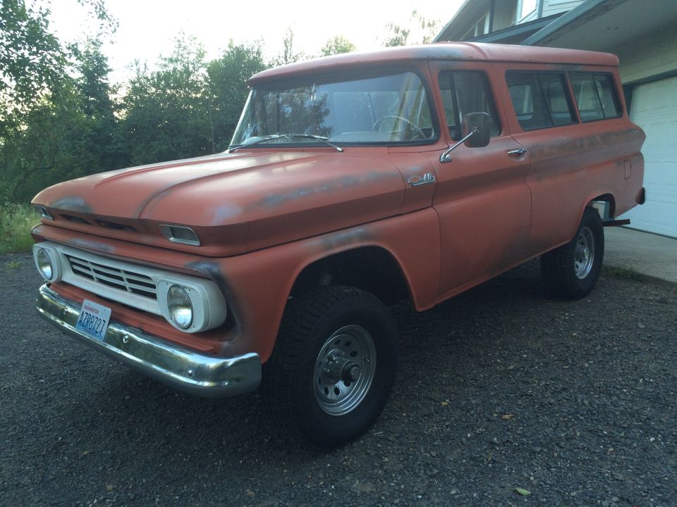1962 Chevrolet Suburban parked in driveway, orange paint faded and showing primer
