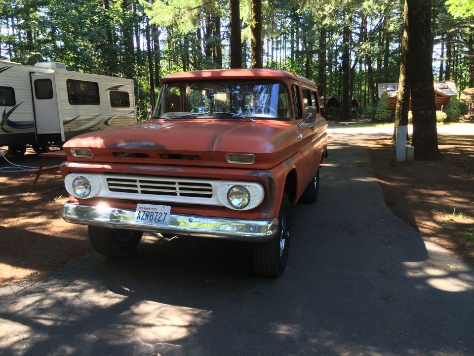 Orange vintage Chevrolet Suburban parked on asphalt driveway, trailer nearby