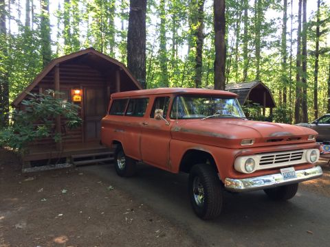 1962 Chevrolet Suburban - This 1962 Chevrolet Suburban is seen parked in a wooded area next to a rustic cabin.