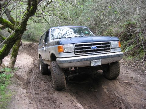 1989 Ford Bronco - Ford Bronco navigates a challenging off-road path with significant mud and uneven terrain.
