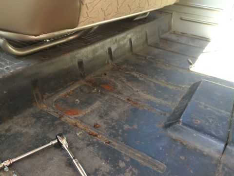 1962 Chevrolet Suburban - Socket wrench rests on the worn interior floor of a vehicle, near a seat with textured fabric.