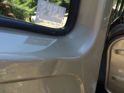 1962 Chevrolet Suburban - A close-up view of a beige vehicle's side panel and window, showing damage and a sticker.