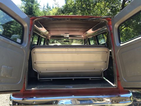 1962 Chevrolet Suburban - The interior of a van is visible with the rear doors open, revealing a folded seat and the cargo area.
