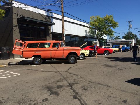 1962 Chevrolet Suburban - Several classic cars are lined up in a parking lot on a sunny day.
