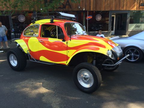1962 Chevrolet Suburban - A brightly painted Volkswagen Beetle, modified for off-road use, is parked on a street next to another vehicle.