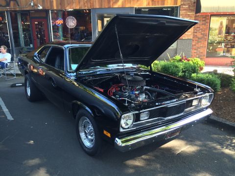 1962 Chevrolet Suburban - A black 1973 Plymouth Duster is displayed with its hood open at a car show.