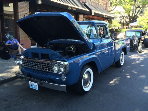 1962 Chevrolet Suburban - A blue 1959 Ford F-100 pickup truck is displayed with its hood open at a car show.