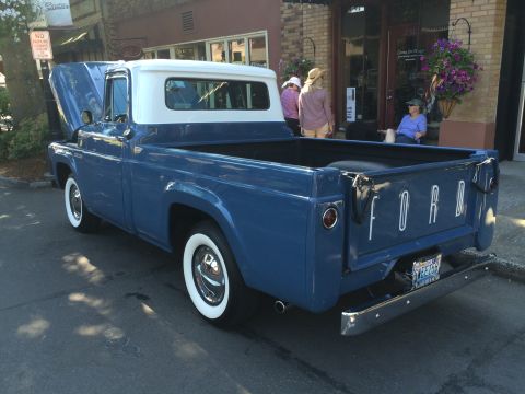 1962 Chevrolet Suburban - A blue and white Ford pickup truck is parked on a street, with its hood up.