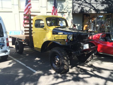 1962 Chevrolet Suburban - A vintage yellow and black flatbed truck is parked at a car show, displayed with American flags.