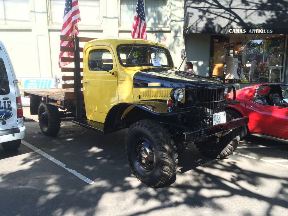 Yellow and black flatbed truck with American flags, parked next to a red sports car