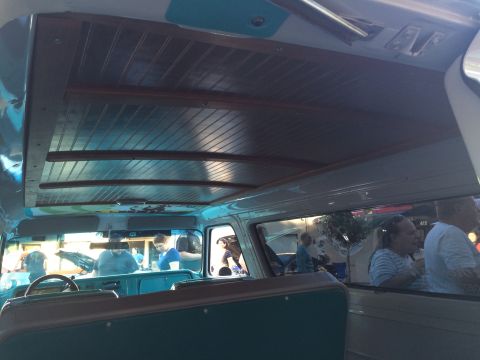 1962 Chevrolet Suburban - The interior of a classic van features a wood-paneled ceiling and turquoise accents, with passengers visible through the windows.