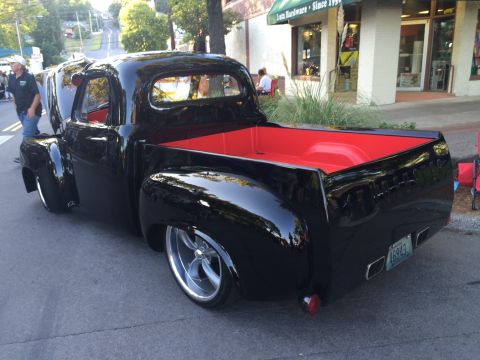 1962 Chevrolet Suburban - Custom black pickup truck with a vibrant red interior and aftermarket wheels is displayed at a car show.