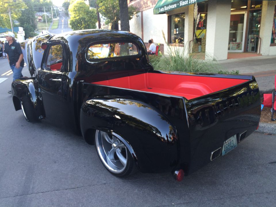 Black pickup truck with red interior and custom wheels, rear view