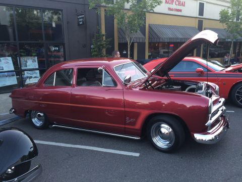 1962 Chevrolet Suburban - A classic red sedan is displayed with its hood open at a car show, parked next to a modern red car.