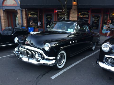 1962 Chevrolet Suburban - A black 1951 Buick sedan is parked on a street in front of a storefront.