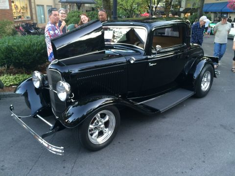 1962 Chevrolet Suburban - A black coupe hot rod is displayed with its hood open, attracting attention from onlookers.