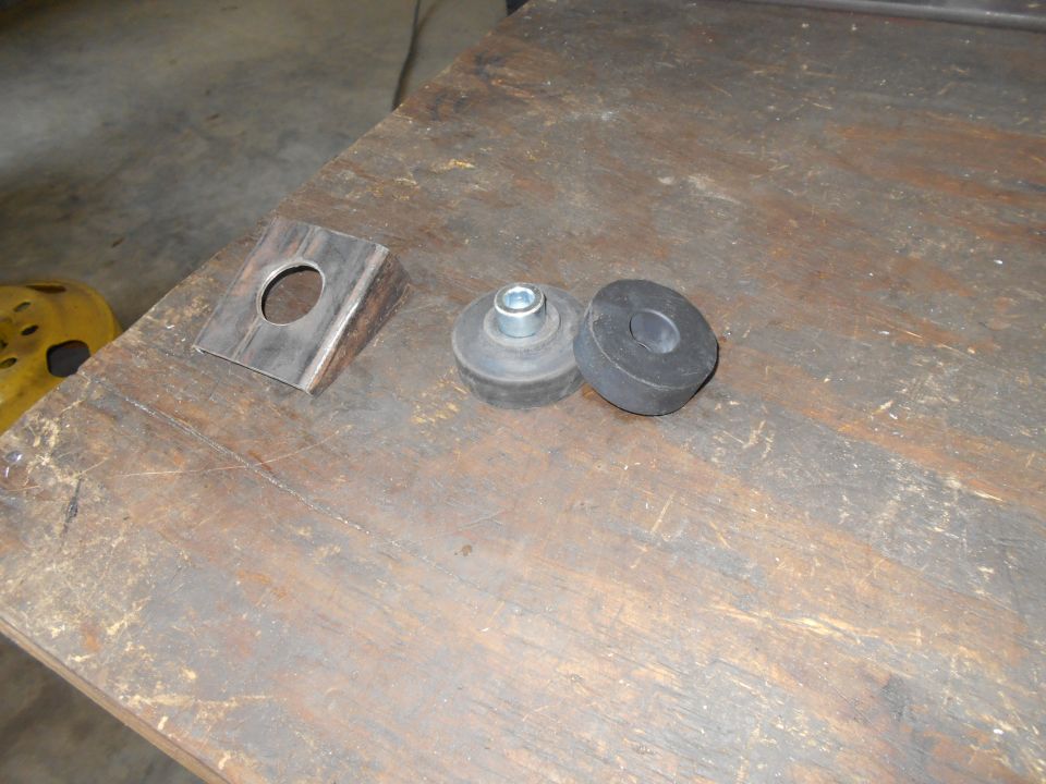 Metal bracket with a hole and two rubber mounts, one with a bolt, on a wooden surface