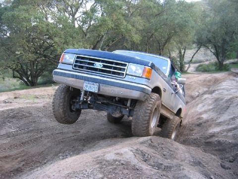 1989 Ford Bronco - A blue Ford F-Series truck navigates a challenging off-road trail with its front wheel lifted.