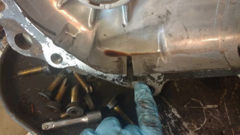 1996 Ford Bronco - A gloved hand points to a seam on a metal transmission housing, with bolts nearby.