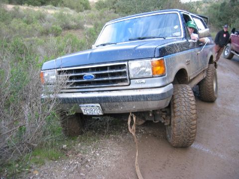 1989 Ford Bronco - Ford Bronco with lifted suspension driving on a muddy off-road trail. Another vehicle is in the background.
